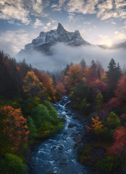 Mountain overlooking a fall-colored forest in the valley and a river going through the valley