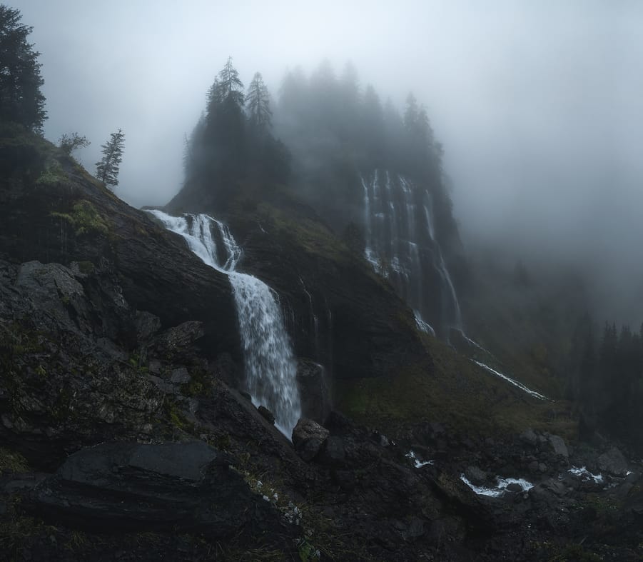 Multiple waterfalls streaming down a valley in a cloudy and moody day
