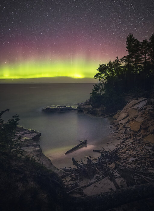 Bright green and magenta northern lights over a beach with rocky cliffs in Michigan