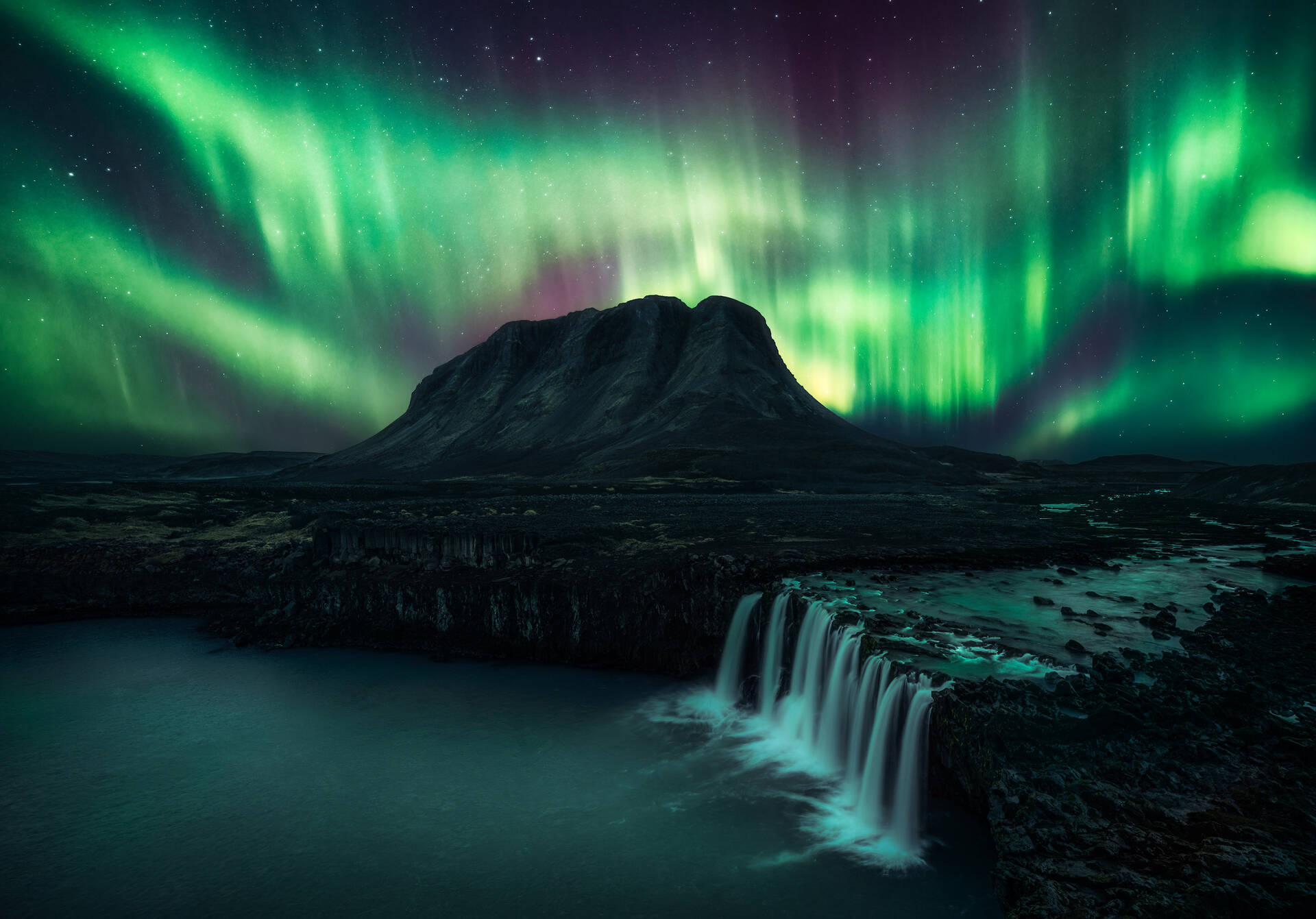 Northern Lights shining with bright green beams over mountain and waterfall