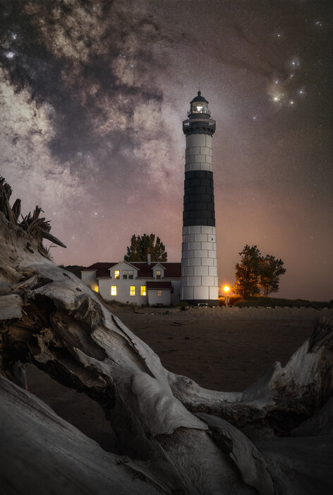 Milky Way core with a lighthouse and a tree trunk in the foreground