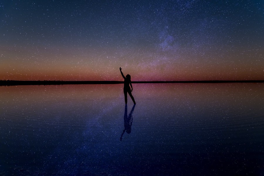 Milky Way and stars reflected over Lake Tyrrell with the silhouette of a woman in the middle of the image