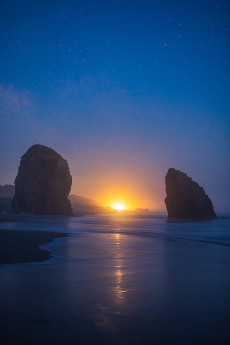 Sea stacks frame the light from the sun during blue hour