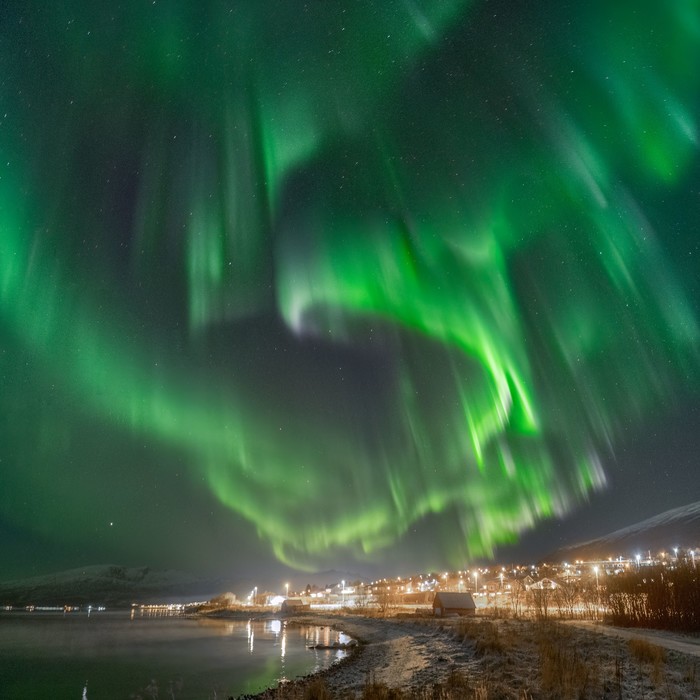 Northern lights shining with intense green colors over a city