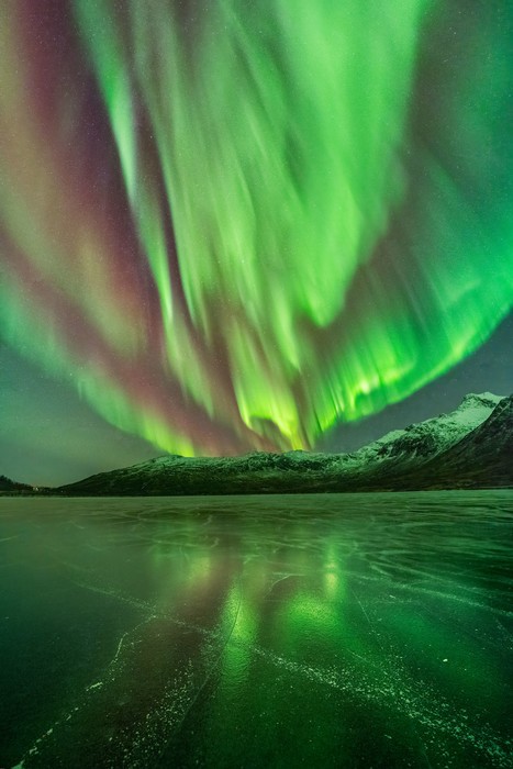 Intense green and red aurora reflecting its light over a frozen lake