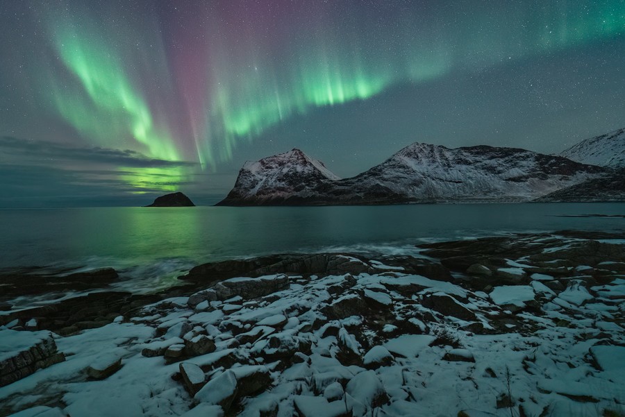 Bright red and green aurora over a mountain in Haukland beach in Lofoten islands