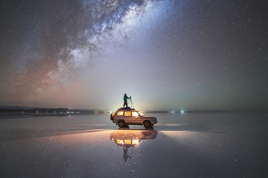 Person standing on an SUV in the middle of salar de uyuni under the night sky with the milky way