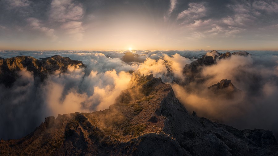 Wide view of mountain tops almost engulfed by dramatic clouds during golden hour