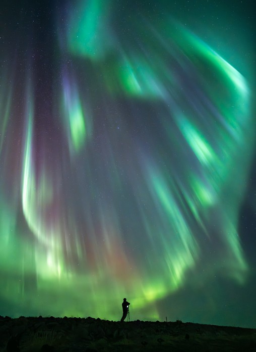 Person taking a photograph under a bright display of Northern Lights