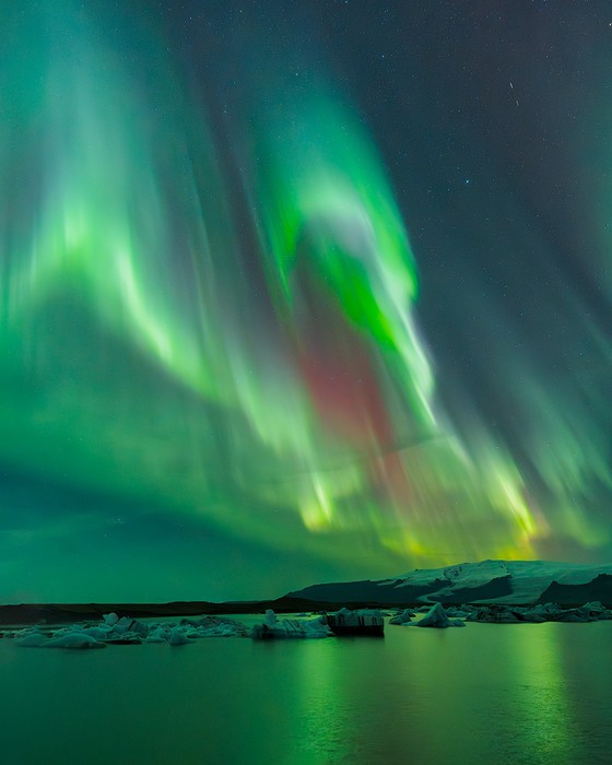 Bright Northern Lights light up a glacier lagoon with icebergs during a night in the fall