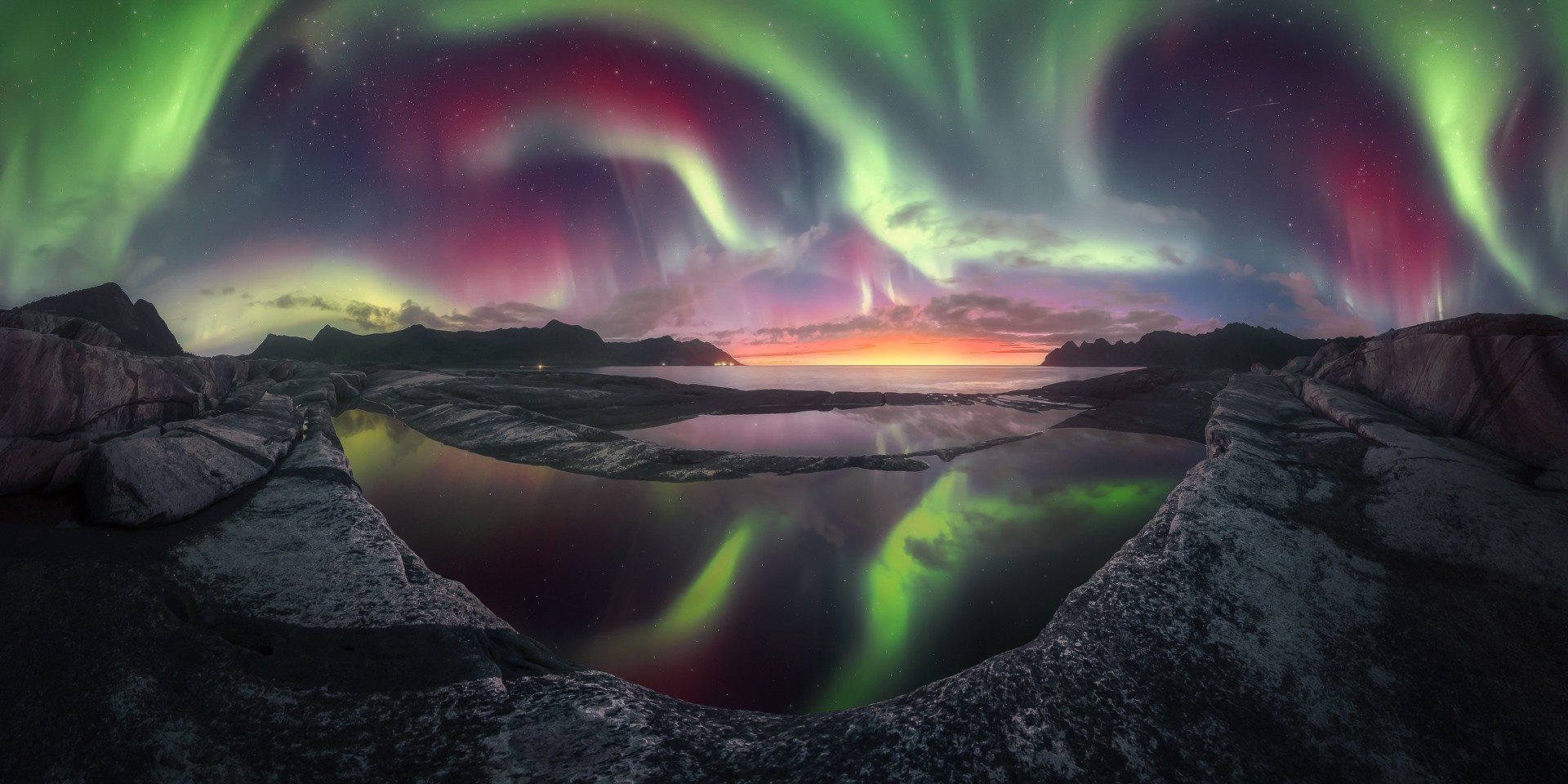 Panorama of the northern lights covering the sky with a reflection in the foreground