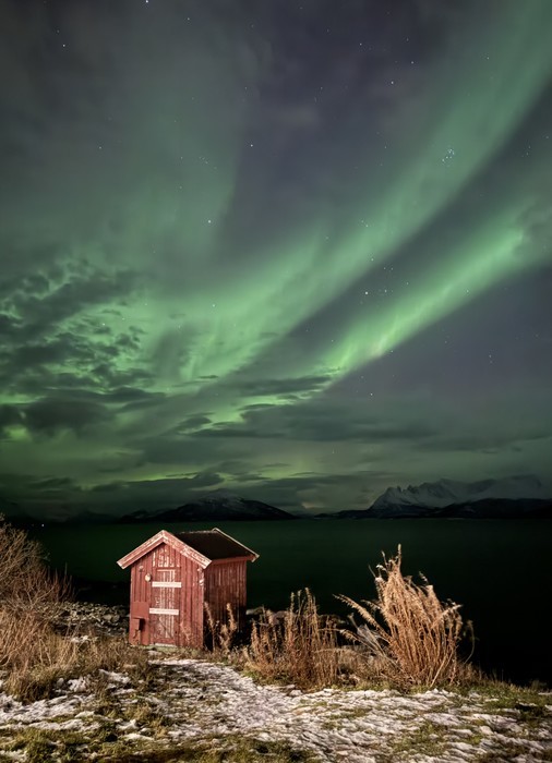 Green Northern Lights covering the sky over a small red cabin