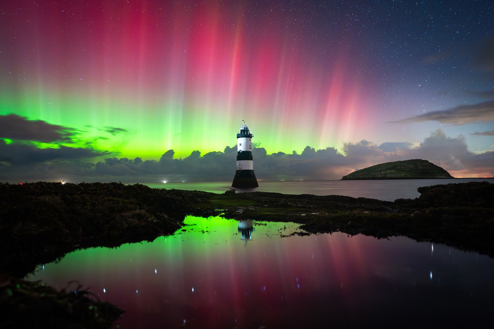 Bright Northern Lights shine in the night sky over a lighthouse