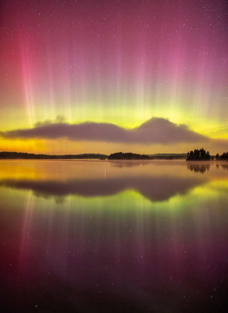 northern lights reflecting on a calm lake with some clouds in the horizon