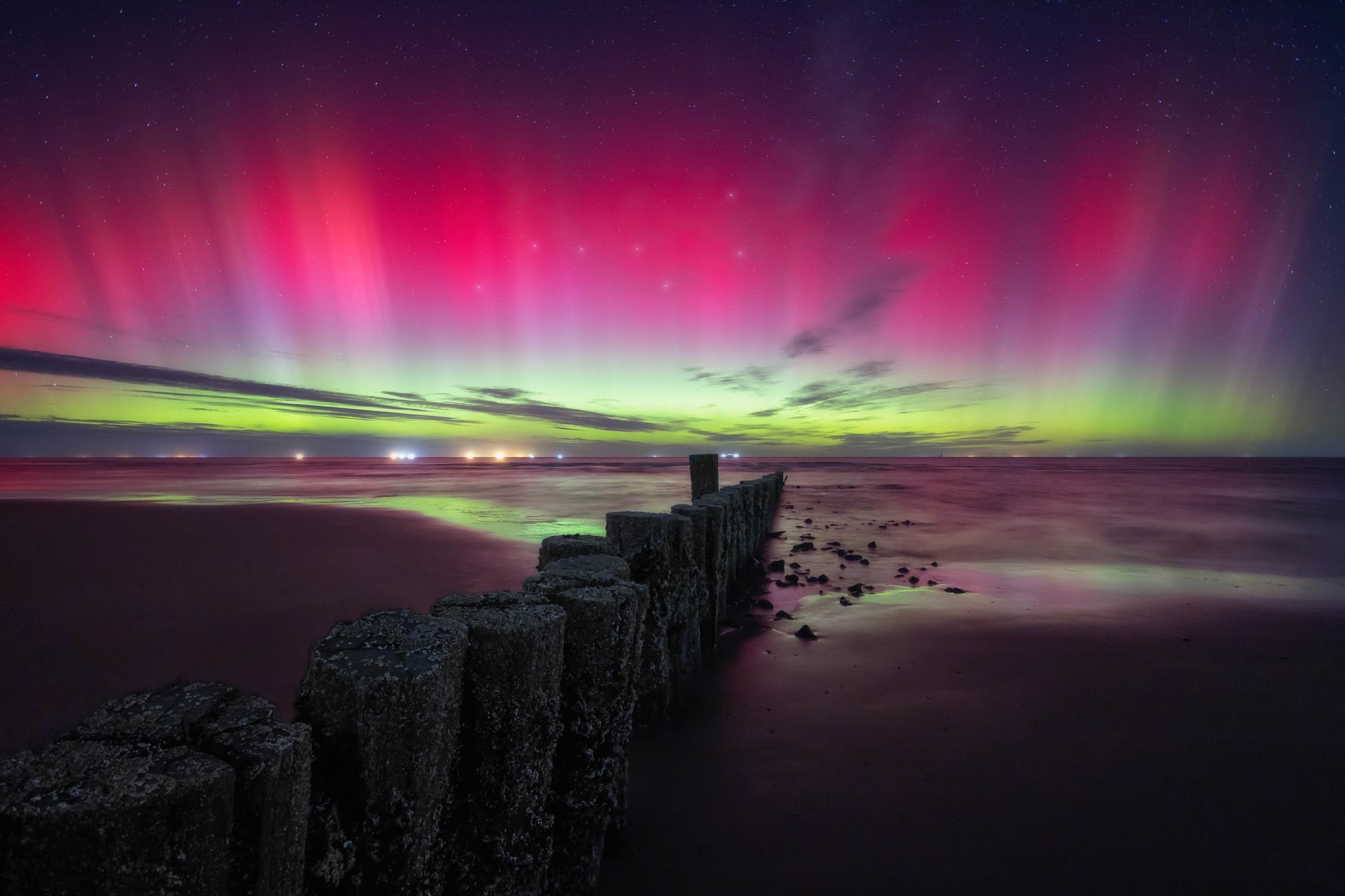 Northern lights with a bright red color on the coast with the big dipper in the sky