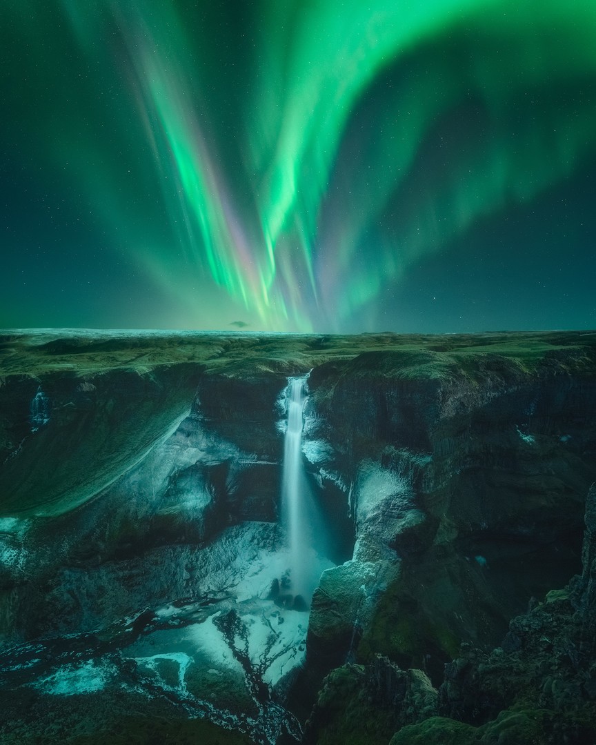 Un noche oscura iluminada por la luz de la Aurora Boreal sobre Haifoss en Islandia