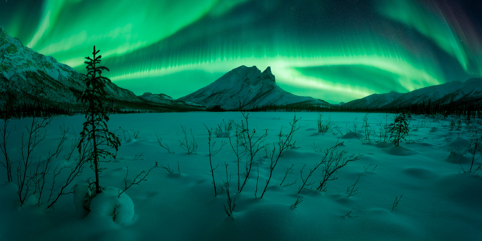 Snow-caped mountain lit up by the northern lights during a winter night
