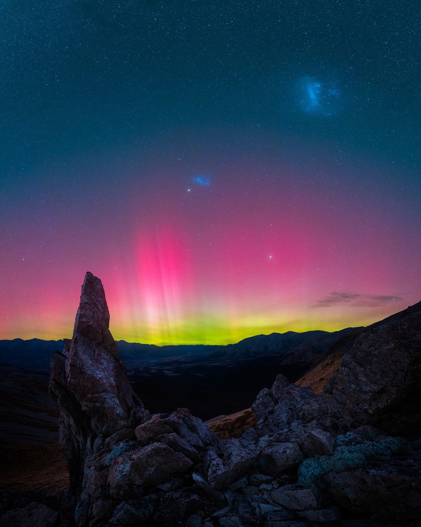 Large and Small Magellanic clouds in the night sky with bright red aurora