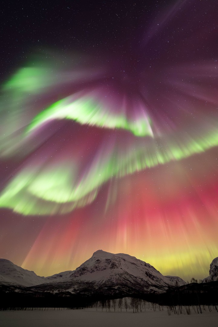 Aurora boreal intensa y brillante cubre la totalidad del cielo sobre una montaña nevada