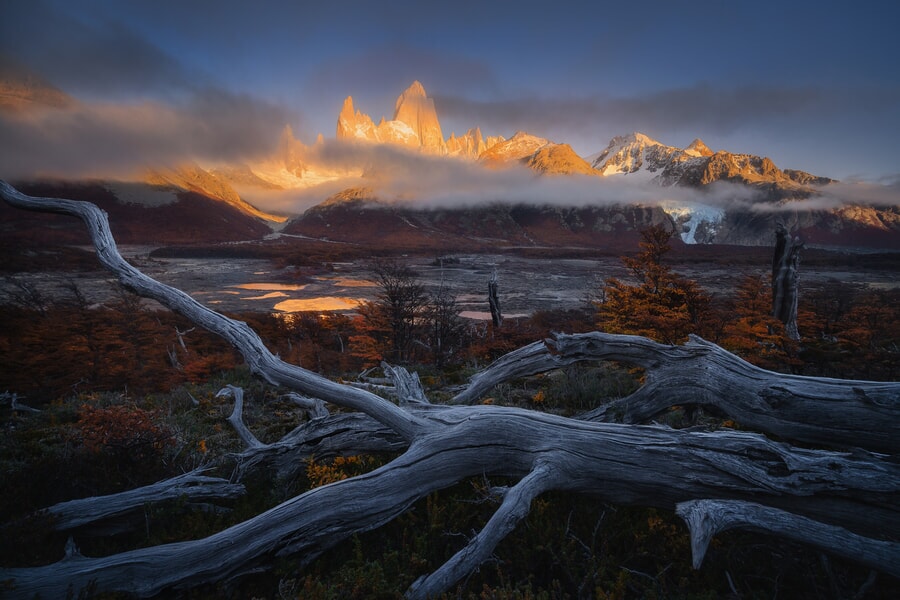 The sun dips below the mountains, silhouetting the trees against a colorful sky