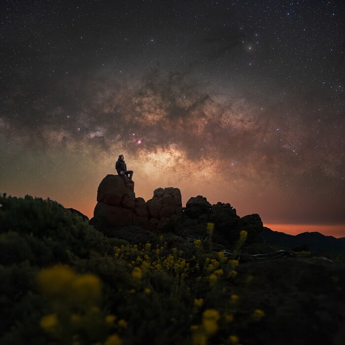 A man on a rock looking up at the expansive night La Palma Photo Tour